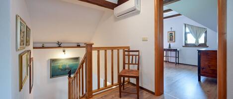 A wooden staircase with a chair, a painting, and an air conditioning unit on the wall.