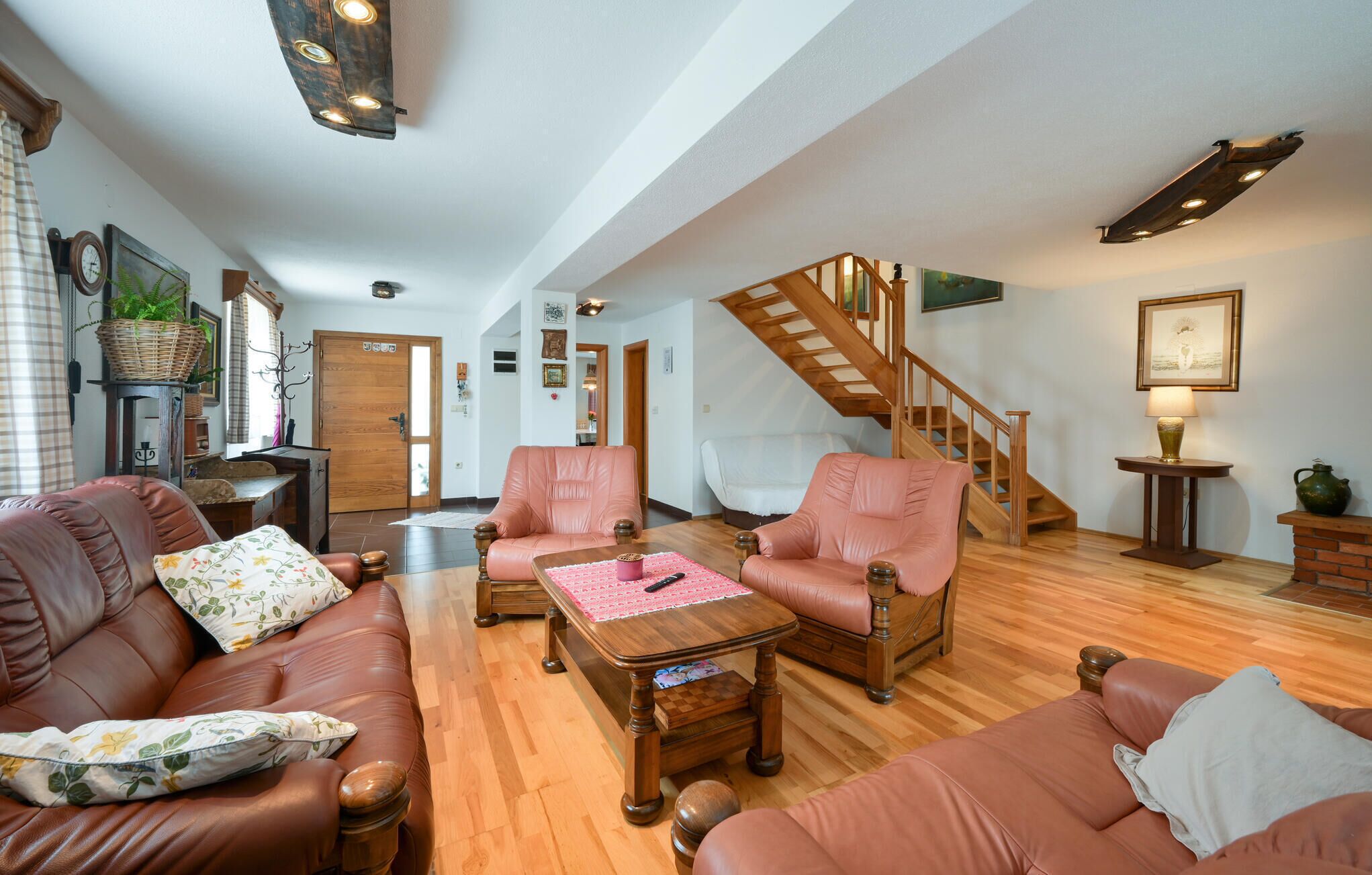 Ein geräumiges Wohnzimmer mit Ledersofas, einem Holztisch und einer Treppe, die zu einer oberen Etage führt.