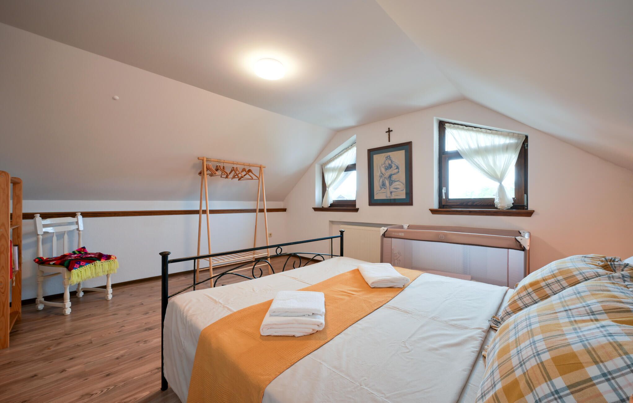 Un dormitorio con cama, una silla de madera, un perchero de madera y una ventana con cortinas.
