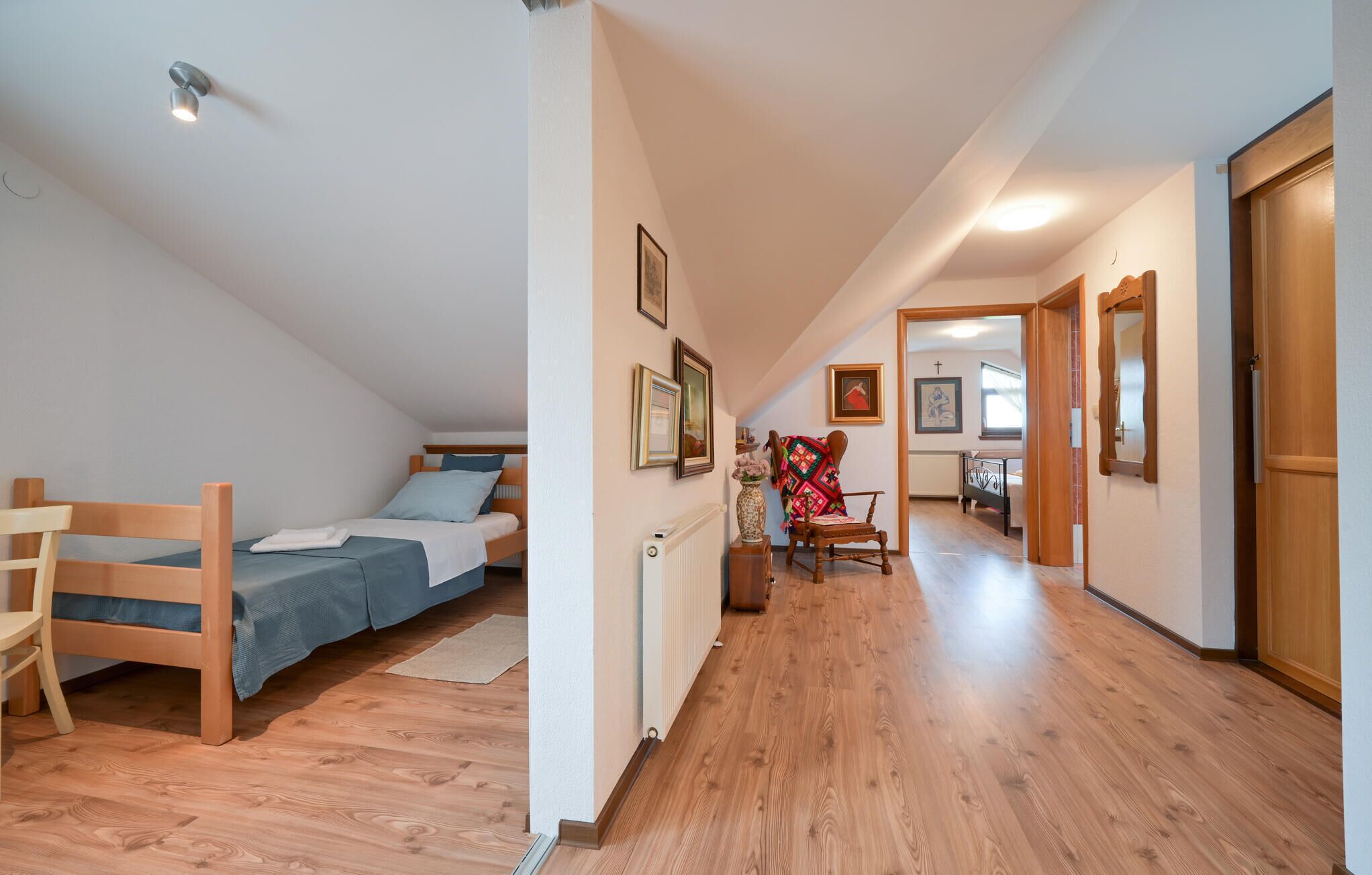 A bedroom with a bed, a chair, and a radiator. There is a hallway leading to another room.