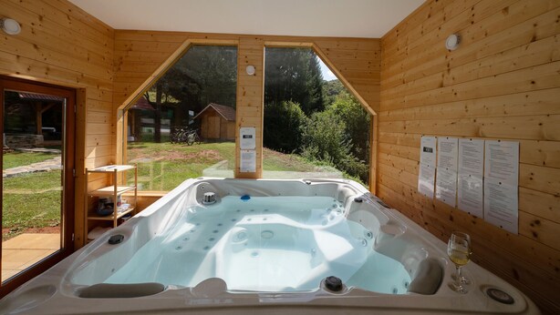 A wooden cabin with a hot tub, a glass door leading outside, and a view of the surrounding forest. - Amazing home in Veselici with sauna (Veselici)