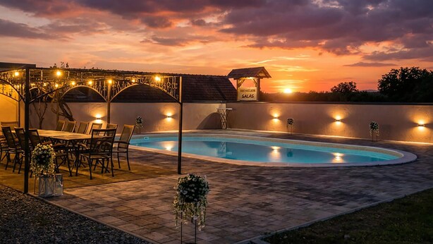 Piscina con vista al atardecer, mobiliario exterior e iluminación con guirnaldas.