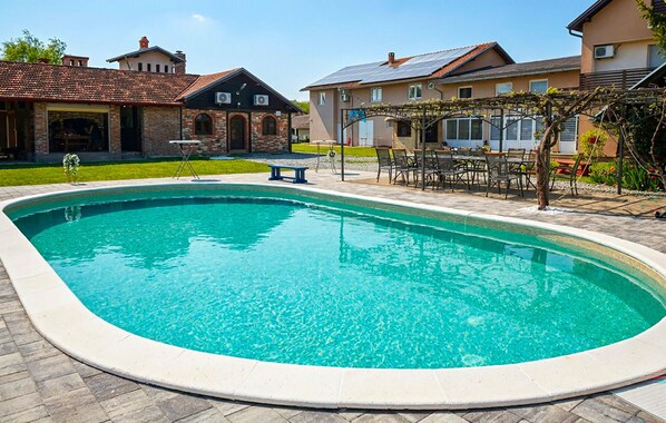 Ein Pool mit einer umlaufenden Terrassenfläche, einer Pergola und angrenzenden Wohnhäusern.