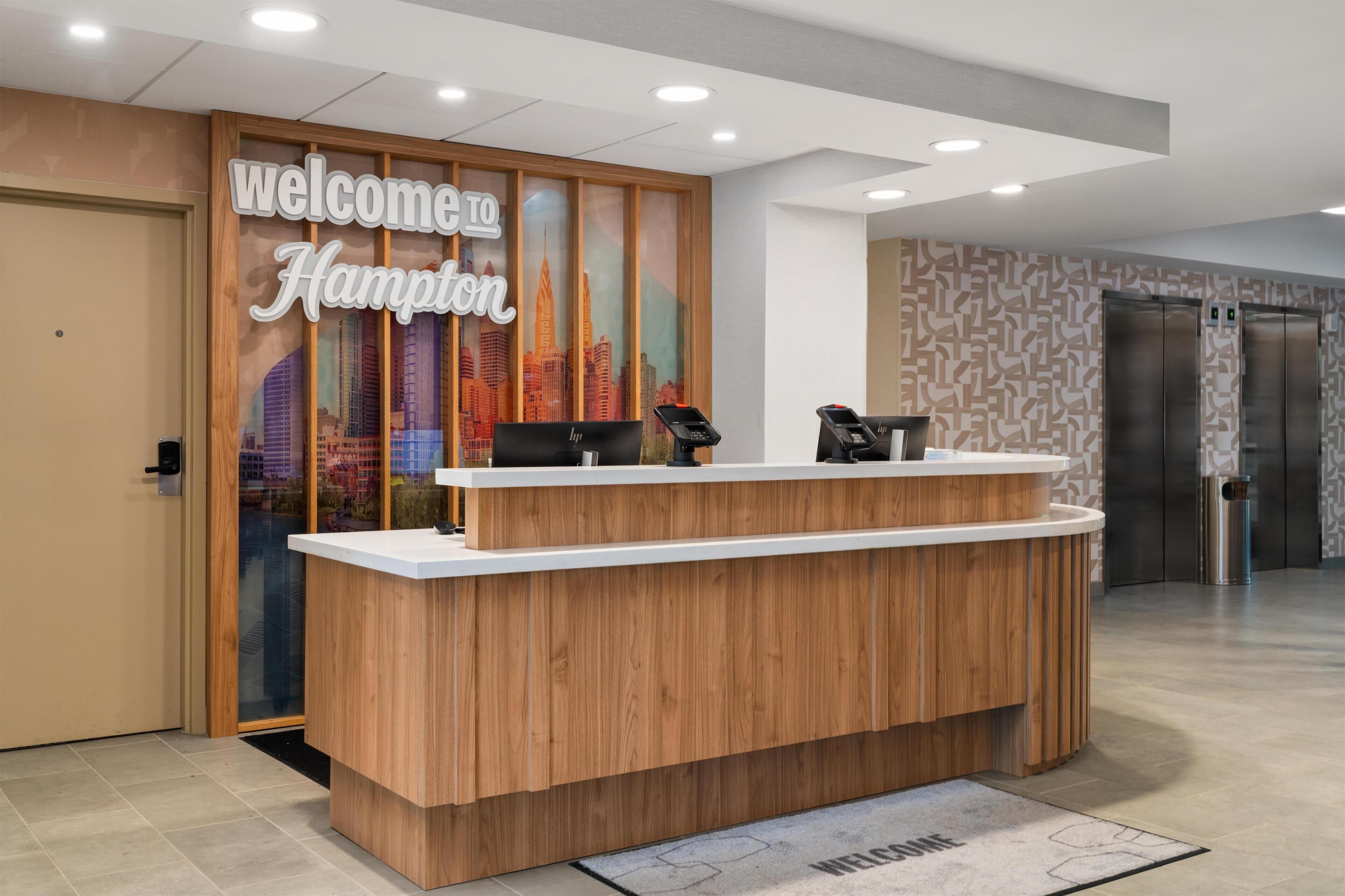 Una recepción con un cartel que dice 'Welcome to Hampton', una computadora, un teléfono y un cesto de basura.