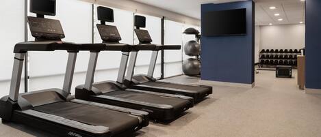 Un gimnasio con cintas de correr, zona de pesas y una pantalla de televisión.