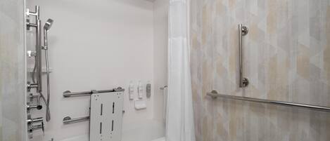 A modern bathroom with a bathtub, shower, and handrails.