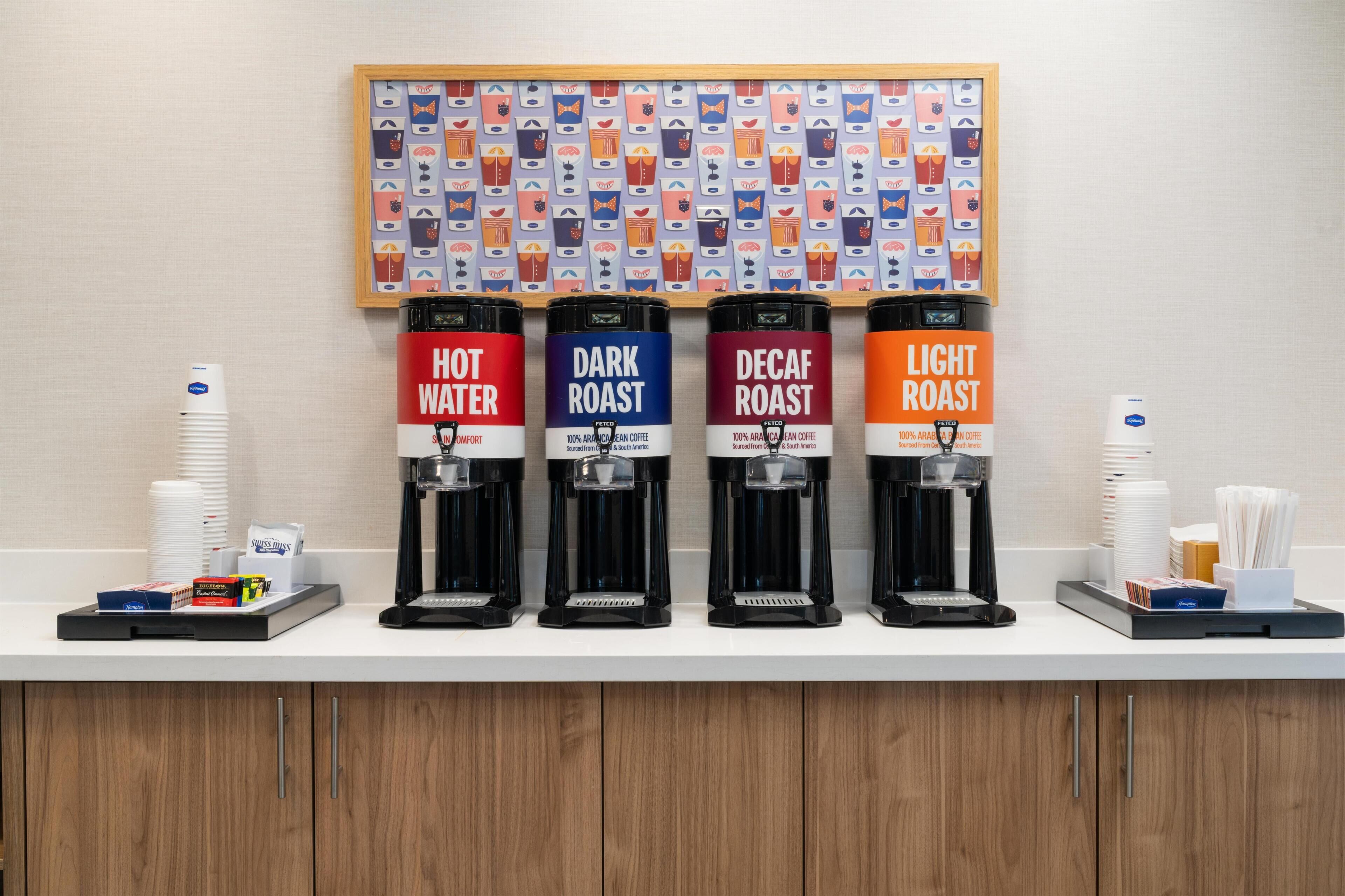 Una estación de café con cuatro dispensadores etiquetados como 'Agua Caliente', 'Tueste Oscuro', 'Tueste Descafeinado' y 'Tueste Claro'.