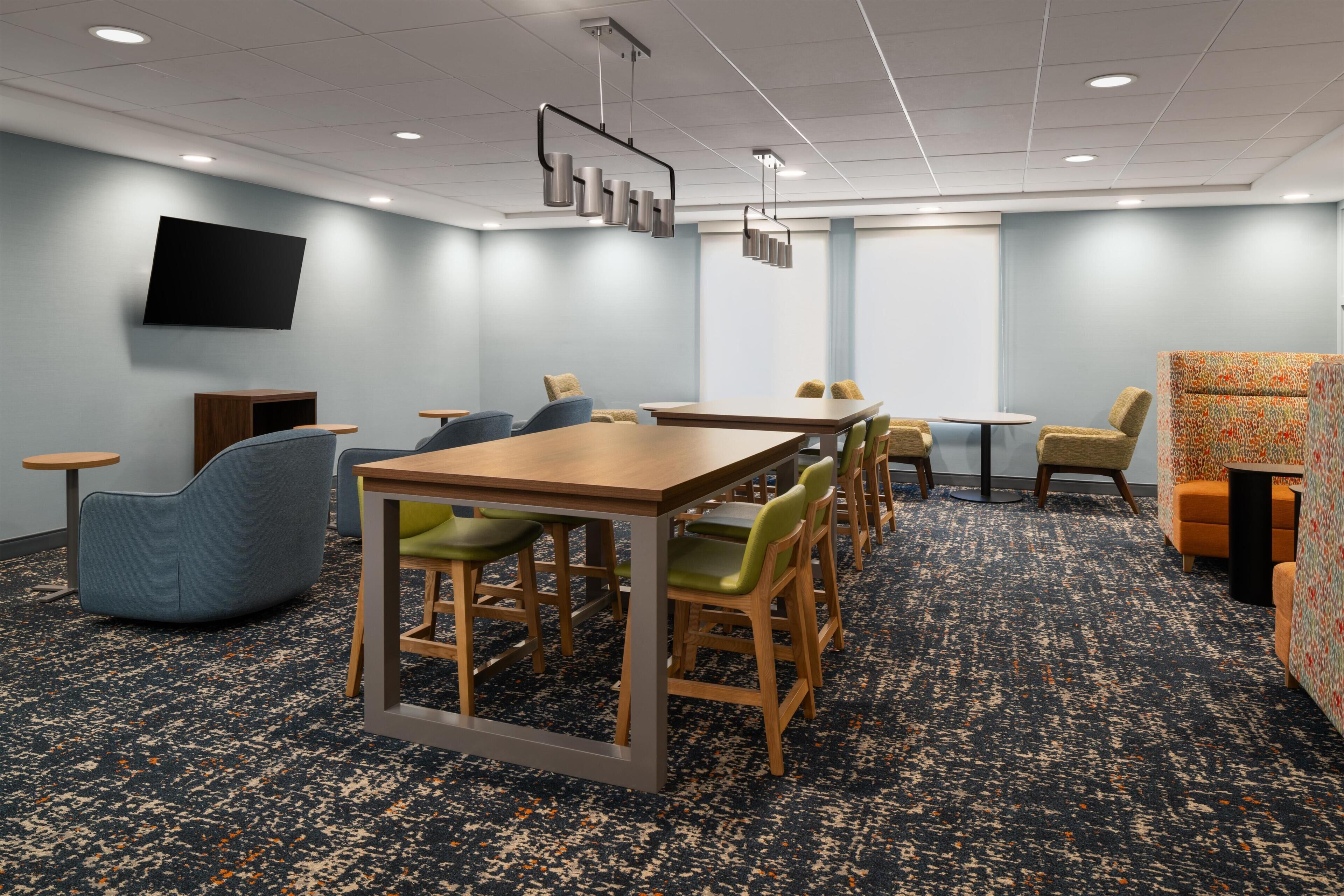 A conference room with a long table, multiple chairs, a flat-screen TV, and a patterned carpet.