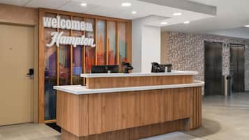 A reception desk with a 'Welcome to Hampton' sign, a computer, a phone, and a trash can.