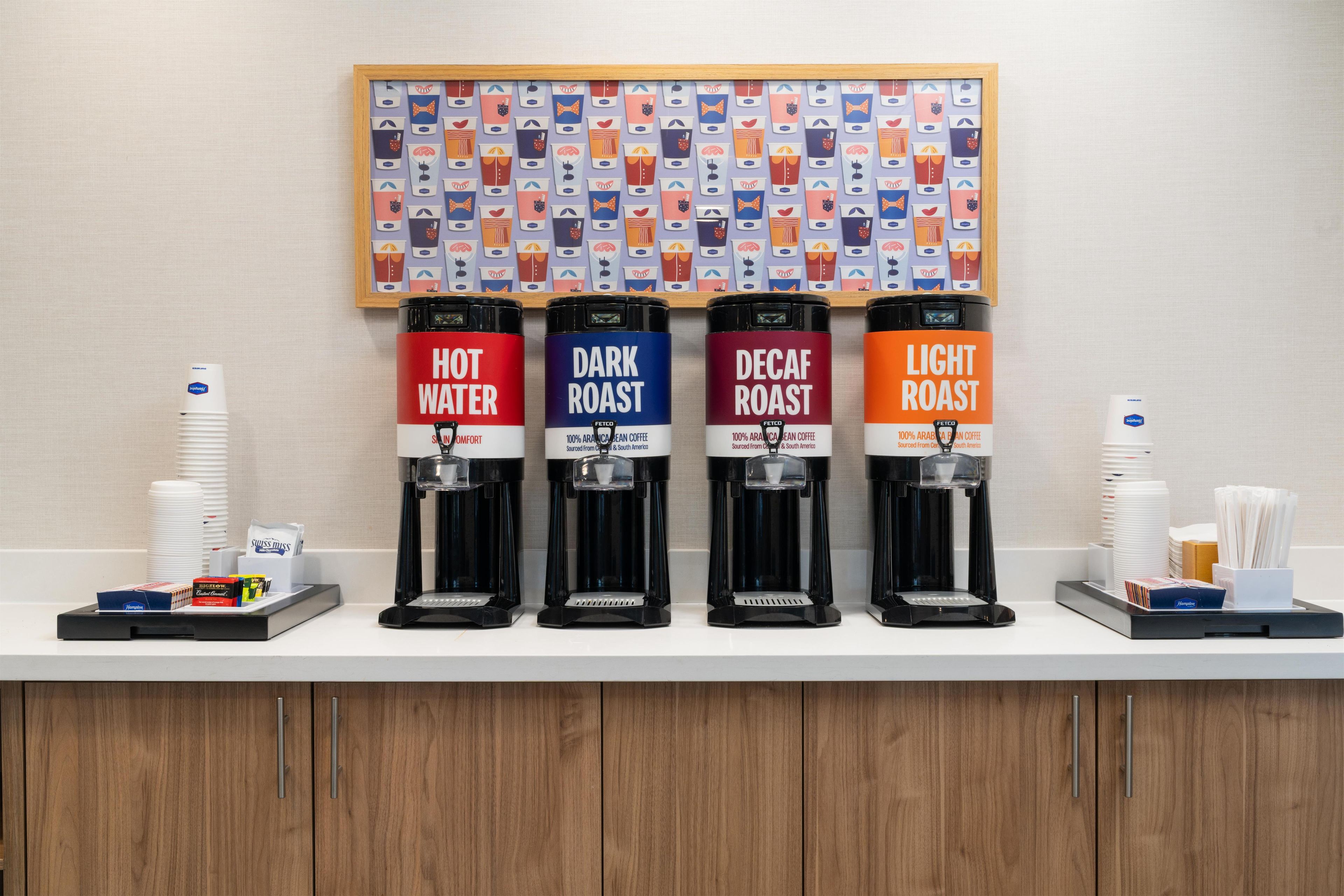 A coffee station with four dispensers labeled 'Hot Water,' 'Dark Roast,' 'Decaf Roast,' and 'Light Roast.'