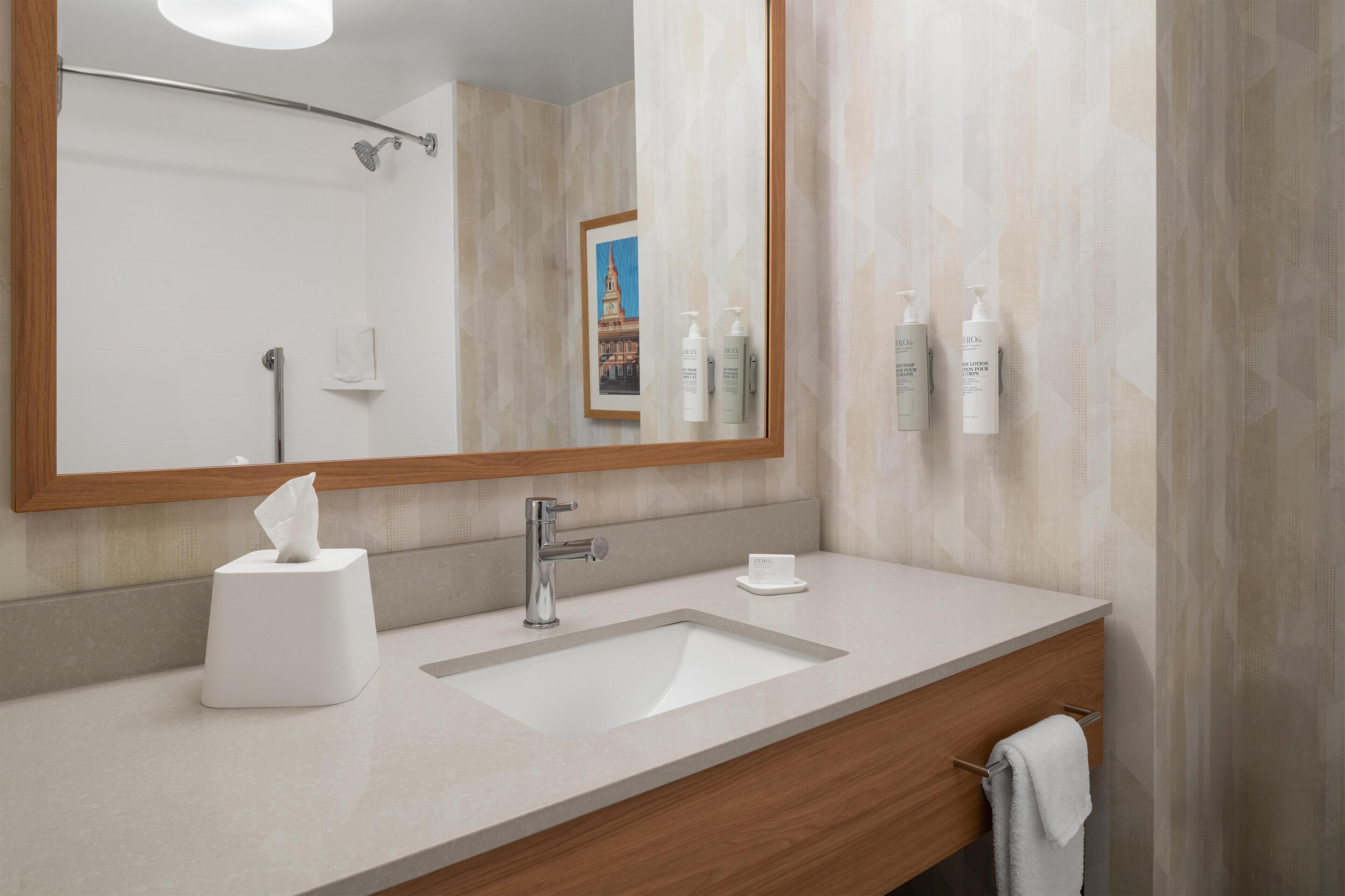 A modern bathroom with a large mirror, a sink, a towel rack, and toiletries on the wall.