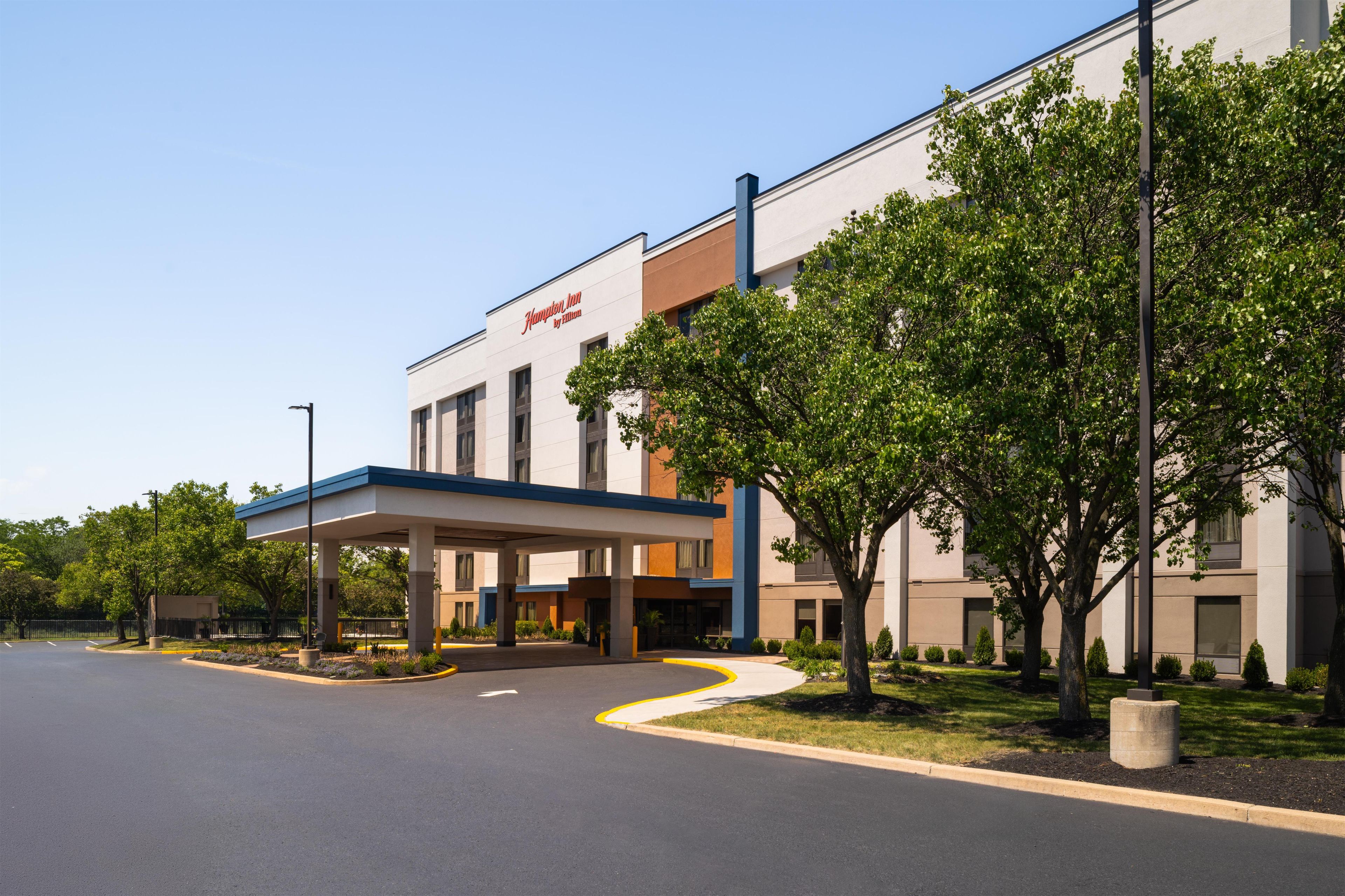 A modern building with a covered entrance, trees, and a clear sky.