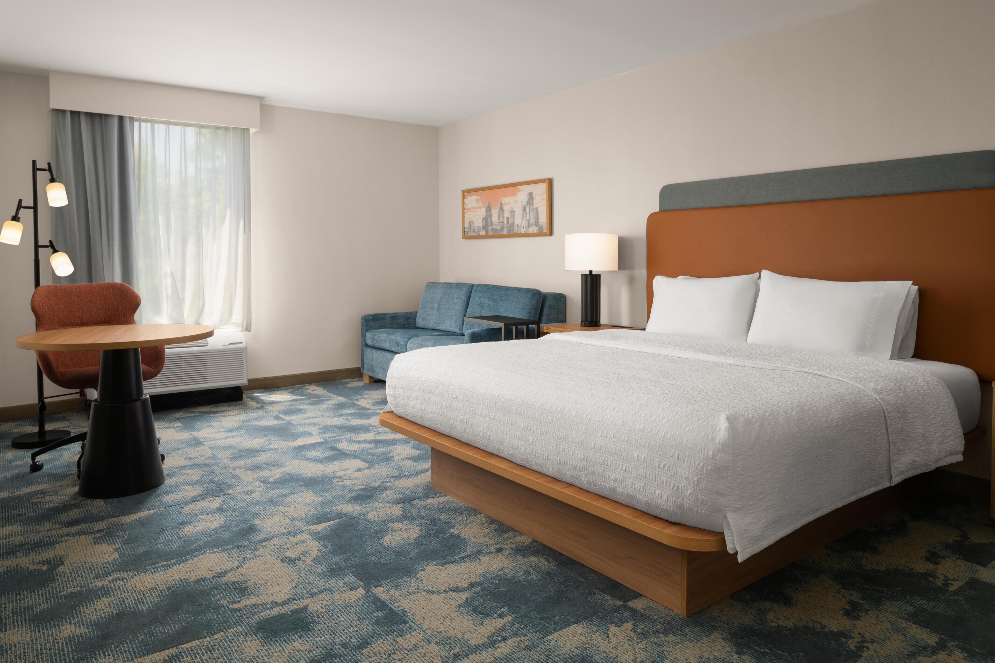 A hotel room with a large bed, a desk, a chair, a lamp, and a painting on the wall.