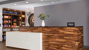 Ein Empfangsschalter mit Holzausstattung, eine Vase mit Blumen und ein Schild, das anzeigt, dass es sich um ein Hilton Hotel handelt.
