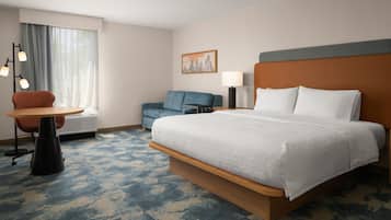 Habitación de hotel con una cama grande, un escritorio, una silla, una lámpara y un cuadro en la pared.