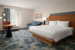 A hotel room with a large bed, a desk, a chair, a lamp, and a painting on the wall.