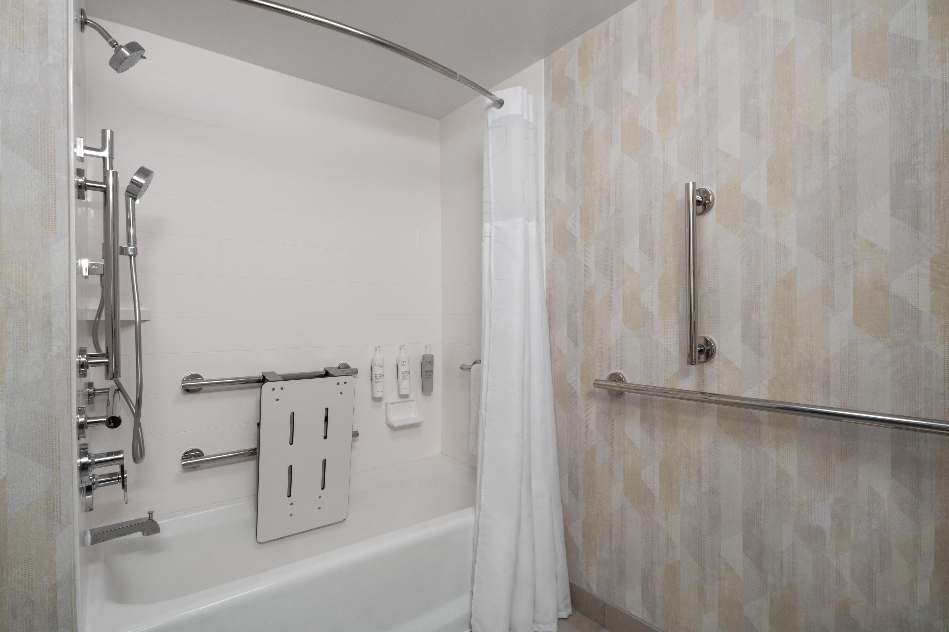 A modern bathroom with a bathtub, shower, and handrails.