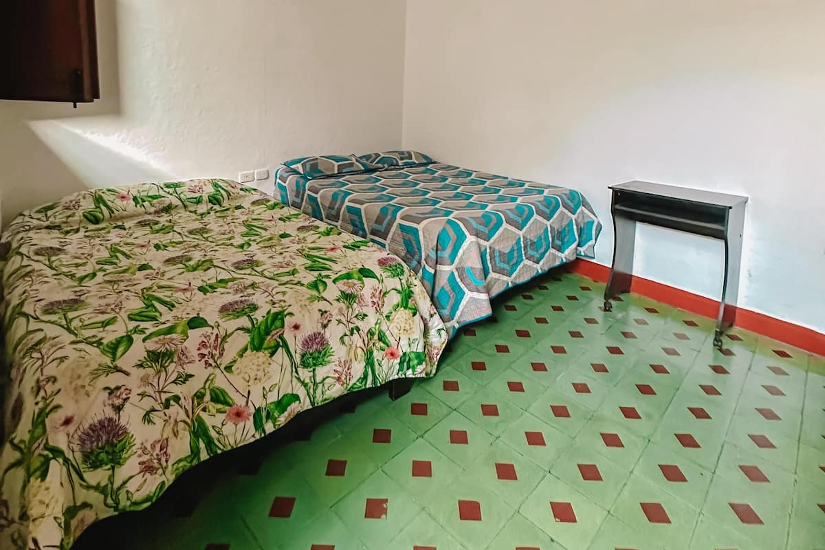 Une chambre avec deux lits, une petite table et un sol carrelé.