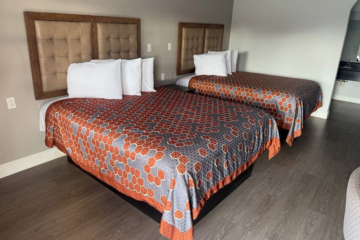 Une chambre d’hôtel avec deux lits, chacun doté d’une tête de lit, et un grand lit recouvert d’une couvre-lit à motifs.