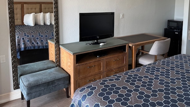 A hotel room with a bed, a TV, a desk with a chair, and a mirror. - WESTERN INN (West Columbia)