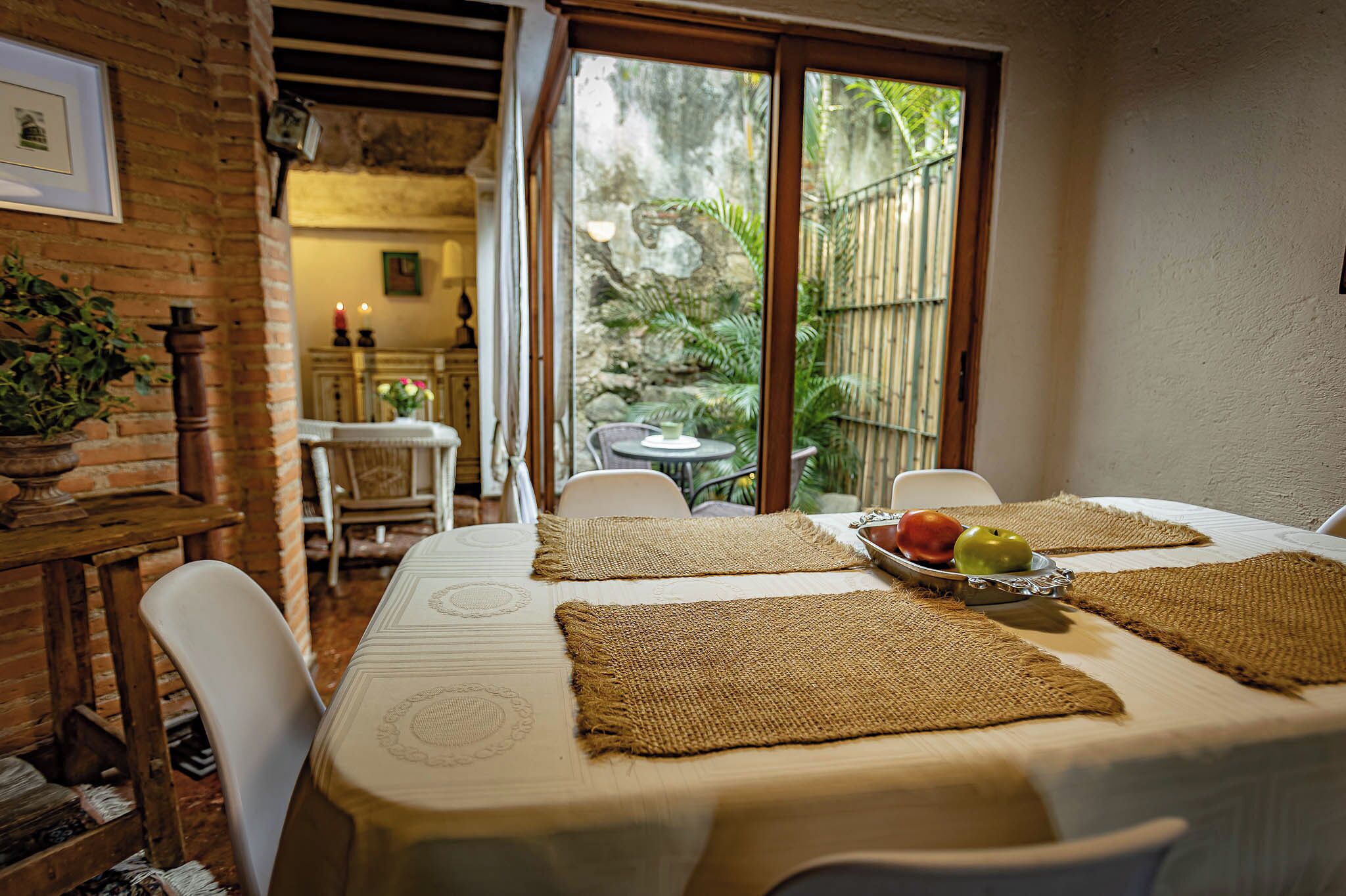 Un comedor con una mesa preparada para dos personas, con individuales tejidos y una bandeja de fruta.