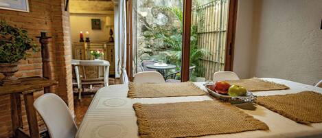 Un comedor con una mesa preparada para dos personas, con individuales tejidos y una bandeja de fruta.