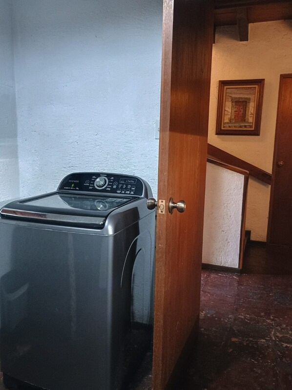 Un lave-linge à chargement frontal se trouve dans une pièce dotée d’une porte en bois et d’un tableau encadré accroché au mur.