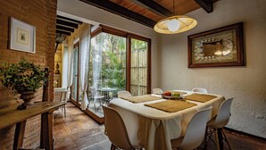 A dining area with a table set for four, surrounded by white chairs, with a view of greenery outside.