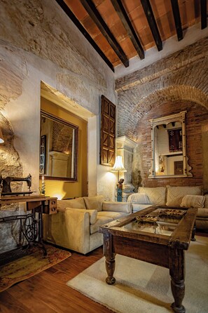 Une pièce au style rustique, avec des murs en briques apparentes, un plafond en bois, une machine à coudre ancienne, un canapé, une table basse et un miroir.