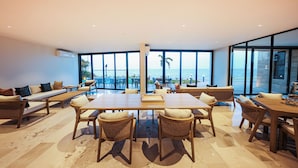 A spacious room with a large dining table, comfortable seating, and large windows offering a view of the sea. - Distrito Puerto - Ocean & Mangrove Views (Puerto Morelos)