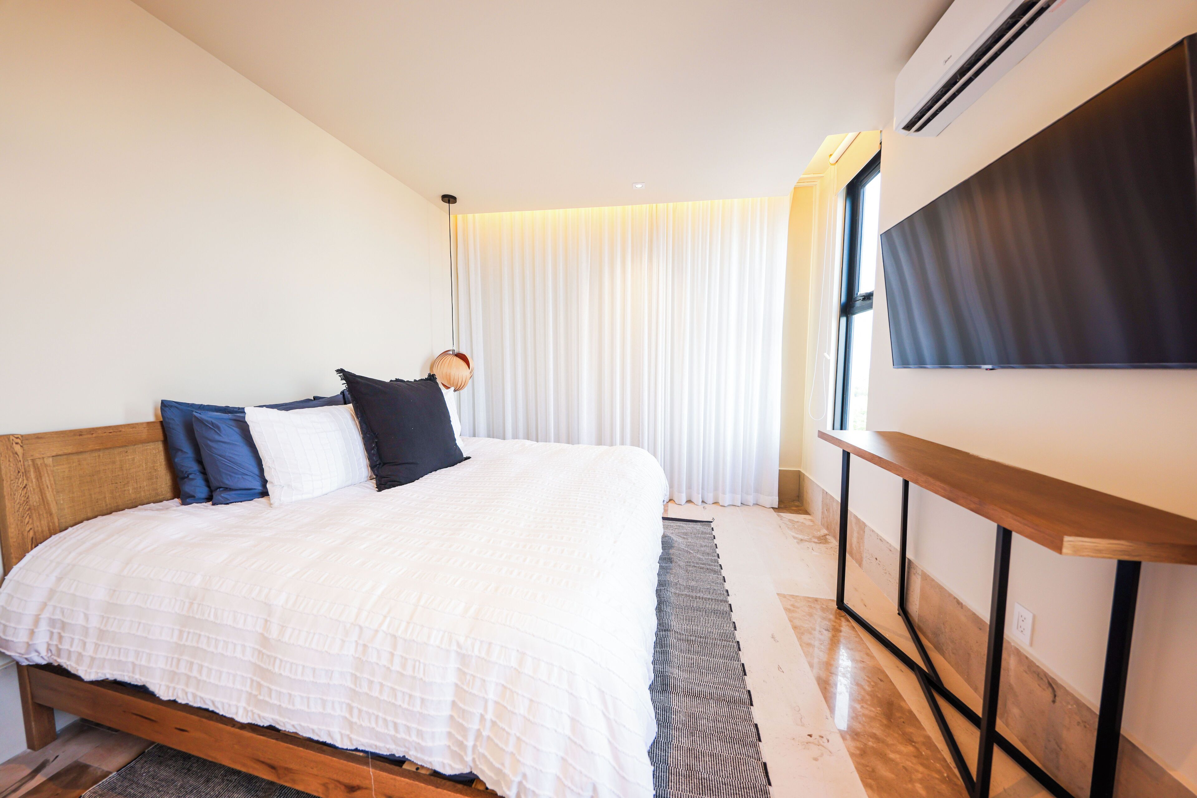 Un dormitorio con cama de madera, ropa de cama blanca, una mesita de noche y un ventanal con cortinas.