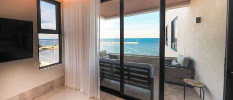A modern hotel room with a large sliding glass door leading to a balcony with a view of the sea.