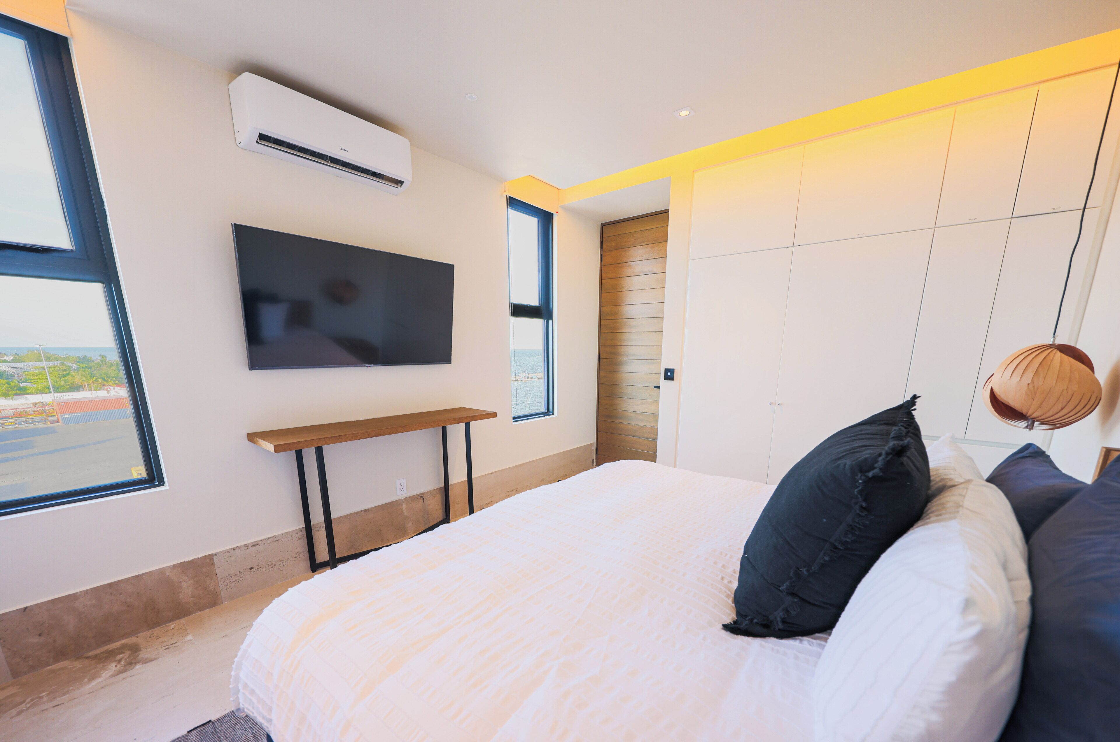A modern bedroom with a bed, a TV mounted on the wall, and a window providing a view.