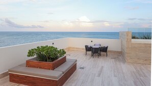 A terrace with a view of the sea, a wooden planter with plants, a table with chairs, and a stone wall. - Distrito Puerto - Ocean & Mangrove Views (Puerto Morelos)