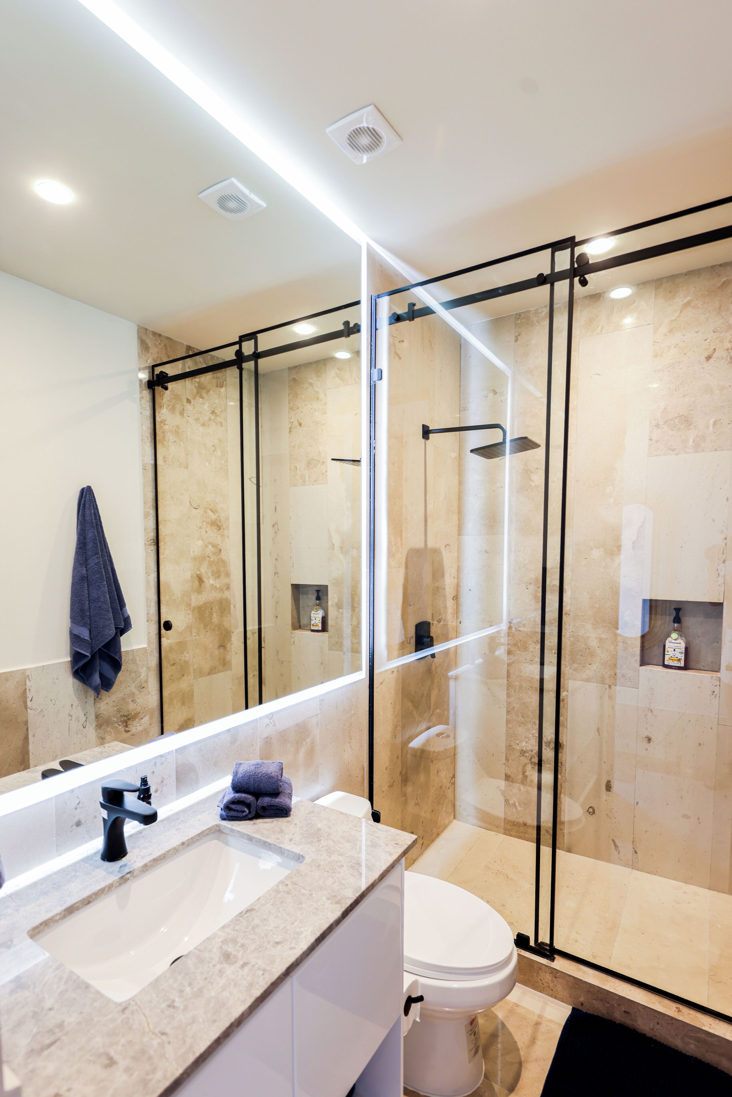 A modern bathroom with a glass-enclosed shower, a sink with a mirror, and a toilet.