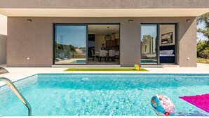 A modern house with a swimming pool, a dining area, and a bedroom visible through glass doors. - Stunning home in Zaton (Zaton)