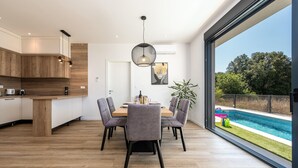 A modern kitchen with wooden cabinets and a dining area with a large window overlooking a swimming pool. - Stunning home in Zaton (Zaton)