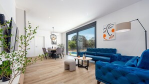 A modern living room with a blue sofa, a dining area with a table and chairs, and a large window offering a view of the outdoors. - Stunning home in Zaton (Zaton)