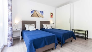 A hotel room with two beds, a nightstand, a lamp, and a painting on the wall.