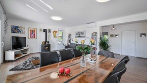 Een moderne woonkamer met een televisie, open haard, eettafel en zitmeubels.
