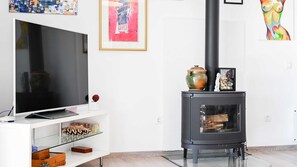 Een moderne woonkamer met een flatscreen televisie, een glazen plank met decoratieve objecten, een zwarte houtkachel en kunstwerken aan de wanden.