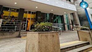 Un moderno edificio de gran altura con fachada curva, varios balcones y una entrada destacada con escalones y un cartel azul.