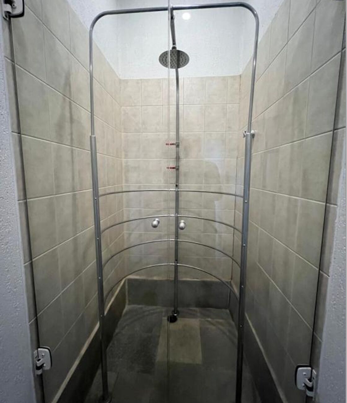 A glass-enclosed shower stall with a curved design, tiled walls, and a visible showerhead.