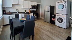 Cocina compacta con armarios blancos, microondas, refrigerador y lavadora y secadora apiladas.
