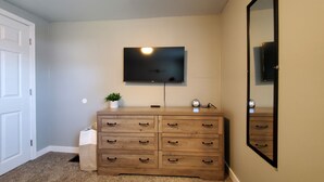 Un dormitorio con un aparador de madera, un televisor montado en la pared y un espejo grande.