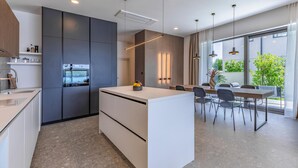 A modern kitchen with a central island, built-in appliances, and a dining area with a view of greenery. - Gorgeous home in Medulin with private swimming pool, can be inside or outside (Medulin)