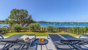 A terrace with two lounge chairs, a table with drinks, and a view of the sea with boats.