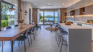 A modern kitchen with a large island, dining area, and a view of the sea.
