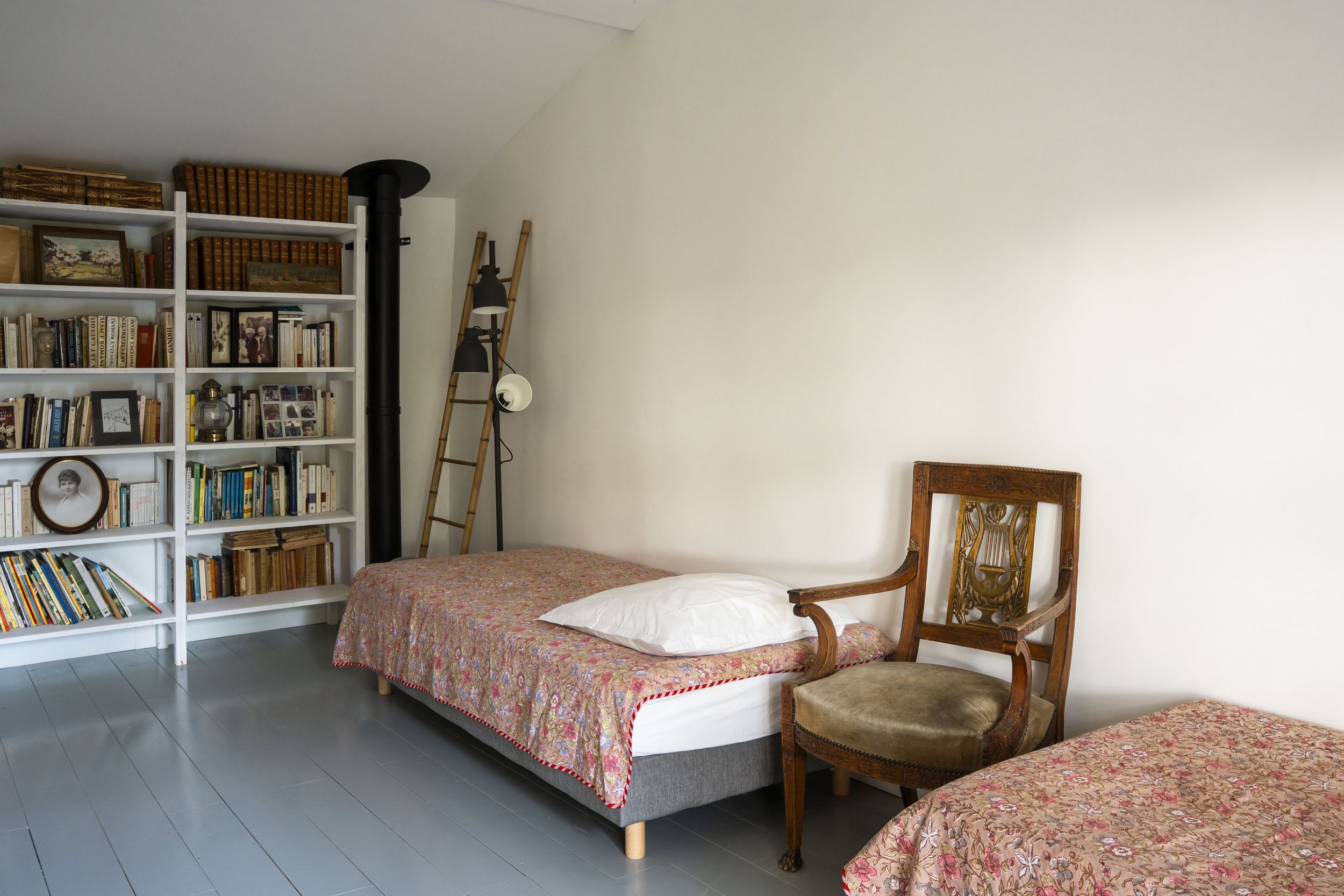 Une chambre à coucher avec un lit, une chaise, une bibliothèque et une échelle.