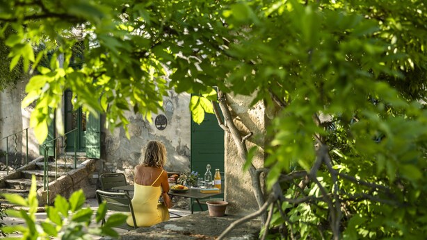 A woman in a yellow dress sitting at a table with a green door in the background. - Comfort Suite for 4 people (Tarascon)